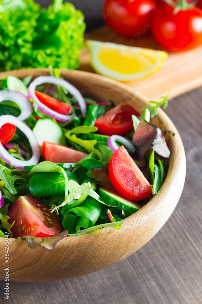 Fresh healthy salad with delicious ruccola, spinach, cabbage, arugula, feta cheese, red onion, cucumber, sesame seeds and cherry tomato on wooden background. Healthy and diet food concept. Fresh healthy salad with delicious ruccola, spinach, cabbage, arugula, feta cheese, red onion, cucumber, sesame seeds and cherry tomato on wooden background. Healthy and diet food concept.
