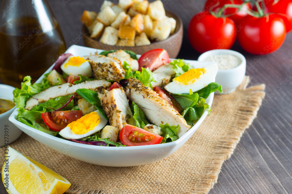 Fresh Caesar salad with delicious chicken breast, ruccola, spinach, cabbage, arugula, egg, parmesan and cherry tomato on wooden background. Oil, salt and pepper. Healthy and diet food concept. Fresh Caesar salad with delicious chicken breast, ruccola, spinach, cabbage, arugula, egg, parmesan and cherry tomato on wooden background. Oil, salt and pepper. Healthy and diet food concept.