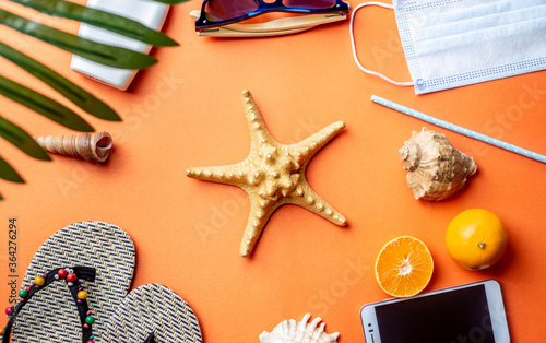 Accessories for beach holidays around a starfish on orange background. Travel to sea and vacation. Top view