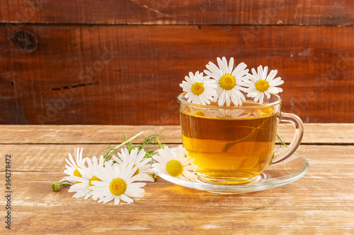 Chamomile medicinal drink in a glass cup on a wooden background. Near daisy flowers.