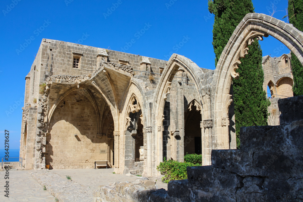 Bellapais Abbey, White Abbey, Abbey of the Beautiful world. Cypress trees behind Gothic arches against a blue sky.