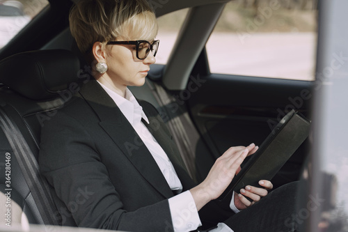 Businesswomanin a car. Lady in a black suit. Woman use a tablet. © prostooleh