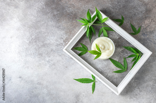 Composition of hemp cosmetic products in a jar and green leaves of plants on a white wooden table background. Natural cosmetic. Cosmetics CBD oil.