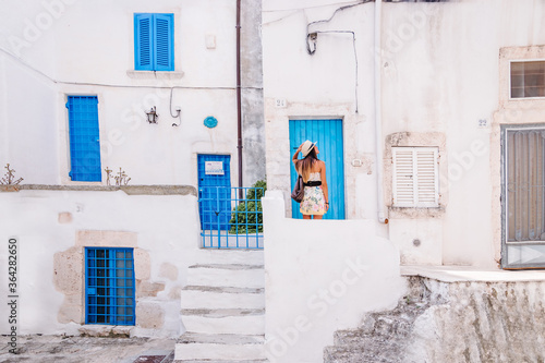 Young woman with straw hat in front of houses with blue door. © Jan Cattaneo