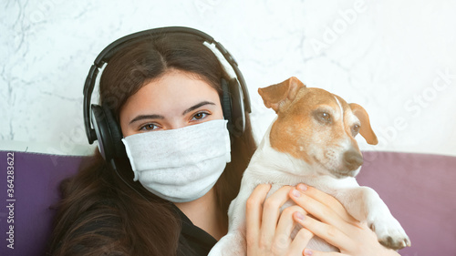 girl in mask with headphones holds dog in arms staying home © Bonsales