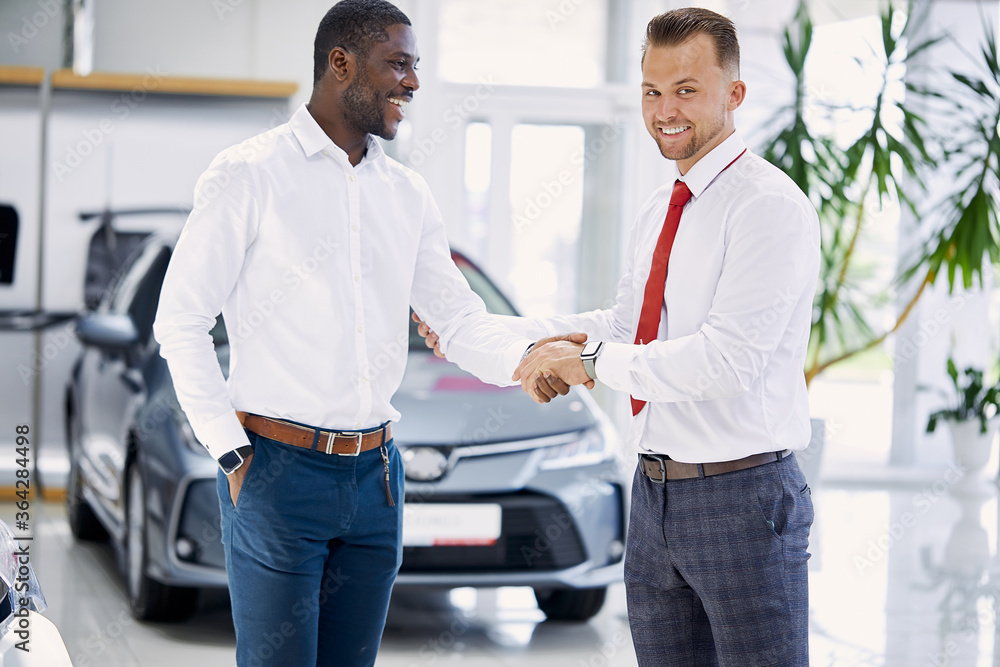 Obraz premium caucasian sales agent and african customer man shaking hands in dealership, they agreed on the sale