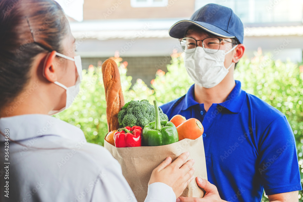 Asian delivery man wearing face mask hand giving bag of food, fruit, vegetable delivery to female customer grocery delivery service during covid19. Asian delivery man wearing face mask hand giving bag of food, fruit, vegetable delivery to female customer grocery delivery service during covid19.