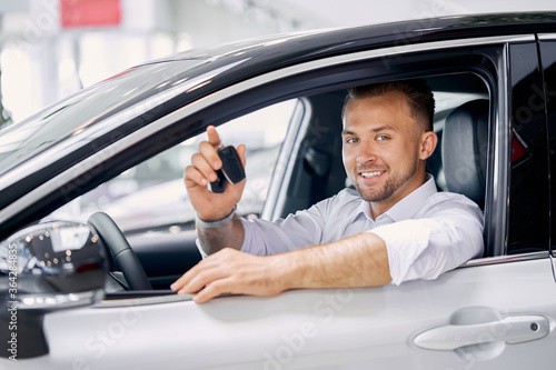 young caucasian man is happy to get keys of auto, he made purchase in modern car showroom © alfa27