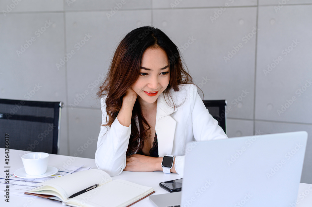 Woman using a laptop computer while sitting on a desk at an office Woman using a laptop computer while sitting on a desk at an office