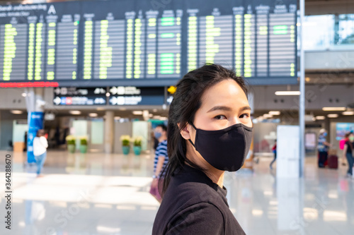 Selective focus at Adult Asian women wearing surgical face mask at Airport terminal in front of Arrival, Departure board. New normal lifestyle for public transport after Covid-19.
