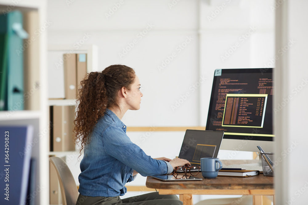 Side view portrait of female IT developer using computer while coding in modern white office interior, copy space - obrazy, fototapety, plakaty 