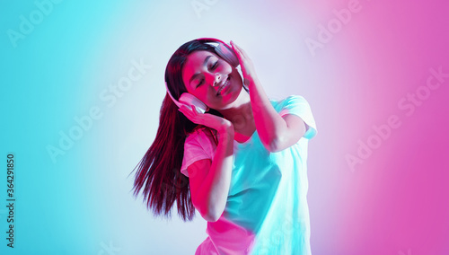 Enjoy dancing. Happy asian girl holds hands on headphones and listens music