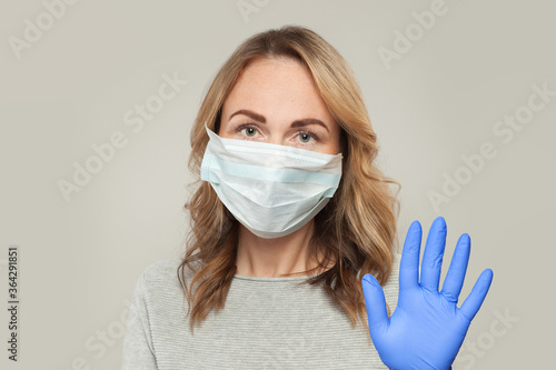 Mature woman in medical protective face mask showing stop gesture on white