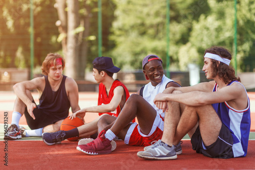 Multiracial basketball team taking break after their game at outdoor arena, blank space © Prostock-studio