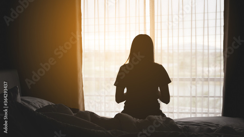 silhouette of alone woman sitting on the bed beside the windows with sunlight in the morning 