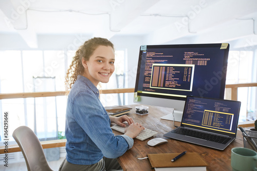Obraz na plátně Portrait of female IT developer smiling at camera while typing on keyboard with