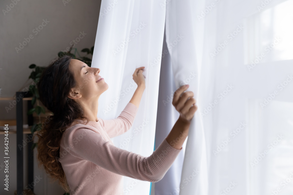 Happy young Caucasian woman open curtains breathe fresh air enjoy early morning sunshine, smiling relaxed millennial female welcome new sunny day, feel optimistic positive, stress free concept Happy young Caucasian woman open curtains breathe fresh air enjoy early morning sunshine, smiling relaxed millennial female welcome new sunny day, feel optimistic positive, stress free concept