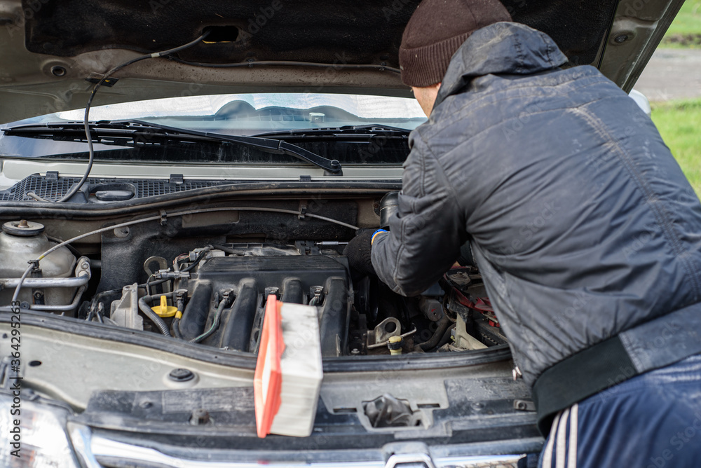 Man is fixing the car. Male hand unscrews an air filter in a car with a screwdriver Man is fixing the car. Male hand unscrews an air filter in a car with a screwdriver