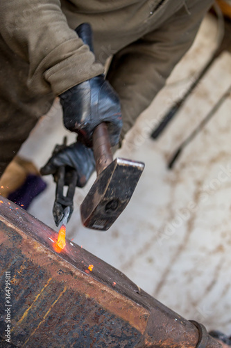 Forging red hot metal with hammer. Selective shallow focus on the melted steel, slow speed picture with motion blurred blacksmith hands and tools. Close-up diagonal view
