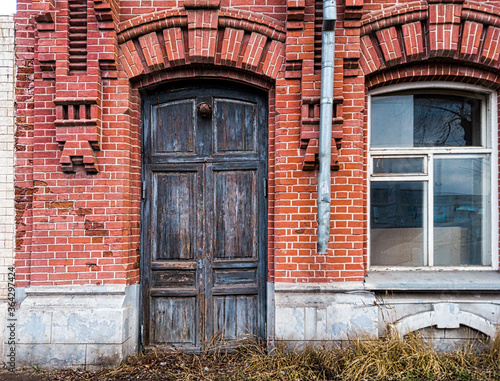 The wooden door in the wall of the old brick building is closed and there is a window nearby © mettus