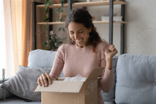 Excited young Caucasian woman open cardboard postal package unboxing internet order at home, happy millennial female client satisfied with good quality order shopping online, delivery service concept