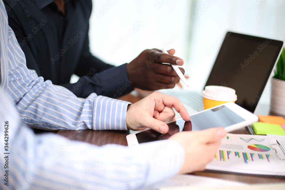 Fototapeta premium Multiracial team working together in office teamwork on laptop analyzing online business project result, focused serious african and caucasian businessmen .looking at computer screen discussing data