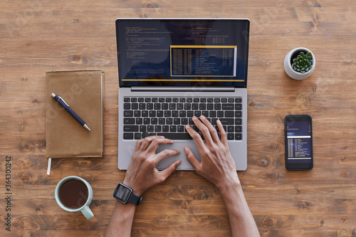 Top down view at male hands typing on laptop keyboard while writing code at textured wooden desk in IT development studio, copy space