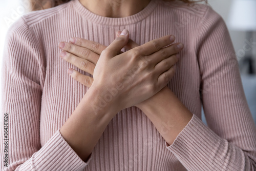 Crop close up of woman hold hands on breast heart show support to sick people, young female feel thankful grateful, demonstrate appreciation and gratitude, volunteer help, healthcare concept photo