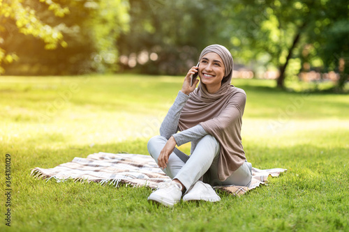 Relaxed arab girl sitting at park and talking on phone © Prostock-studio