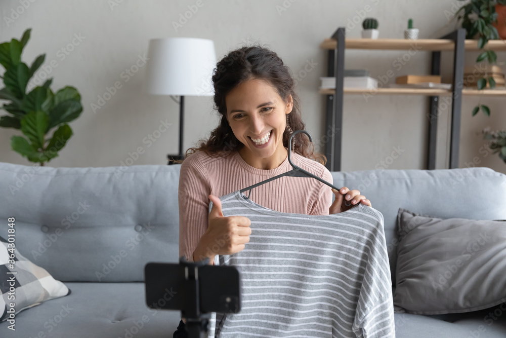 Smiling Caucasian girl influencer vlogger record clothes unpacking on smartphone camera at home, happy young woman stylist blogger recommend apparel, satisfied with online shopping in internet Smiling Caucasian girl influencer vlogger record clothes unpacking on smartphone camera at home, happy young woman stylist blogger recommend apparel, satisfied with online shopping in internet