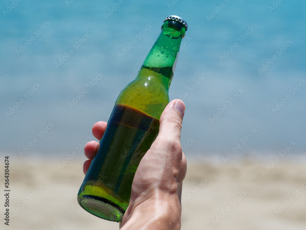 Vacation concept. Male hand holding new bottle of beer on the ocean beach.. Vacation concept. Male hand holding new bottle of beer on the ocean beach..