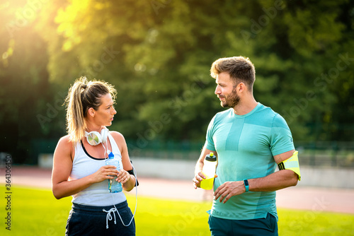 Happy athletic couple communicating after training on water break in park