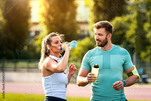 Handsome healthy couple on water break during training in park