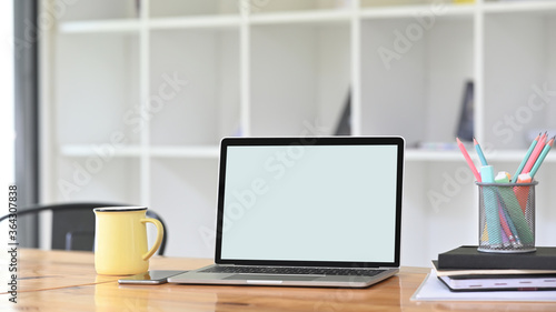 A comfortable workspace is surrounding by a white blank screen computer laptop and office equipment.