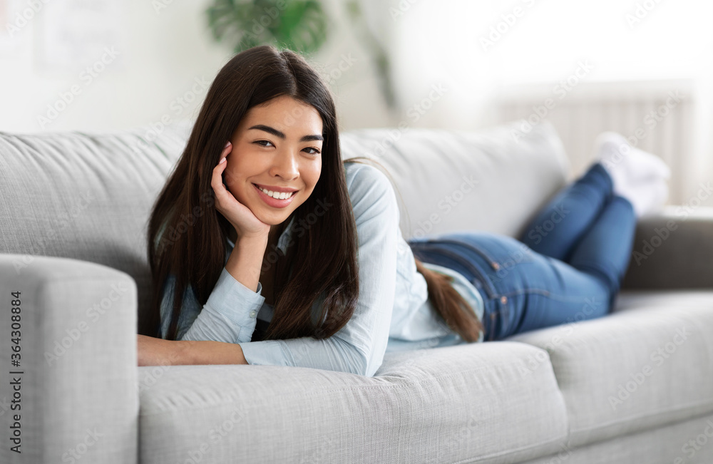 Smiling Young Asian Girl Resting On Comfortable Couch and Posing To Camera Smiling Young Asian Girl Resting On Comfortable Couch and Posing To Camera