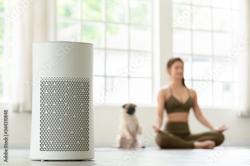 Air purifier in cozy white Living room for filter and cleaning removing dust PM2.5 HEPA at home with woman exercise yoga with dog in background,for fresh air and healthy life,Air Pollution Concept photo