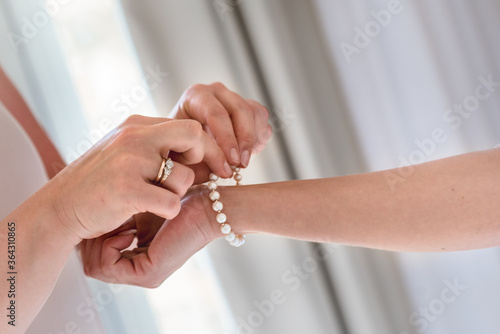 Bridesmaid is helping bride to put on pearl bracelet, moring wedding preparations