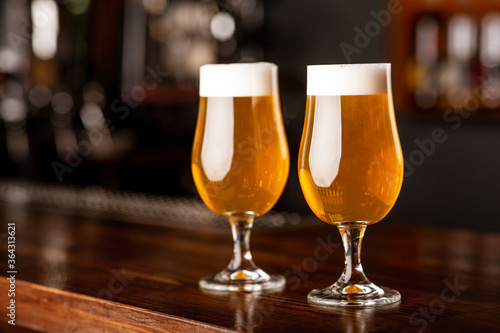 Light beer for clients. Two glasses on wooden bar counter in blurred interior