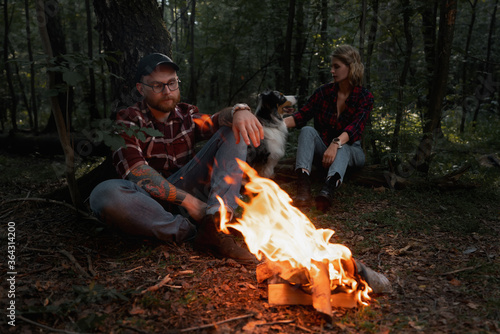 Beautiful Backpacker Woman And Man Having Rest Near Bonfire After Strolling And Hiking In Forest With Aussie Australian Breed Dog © Akaberka