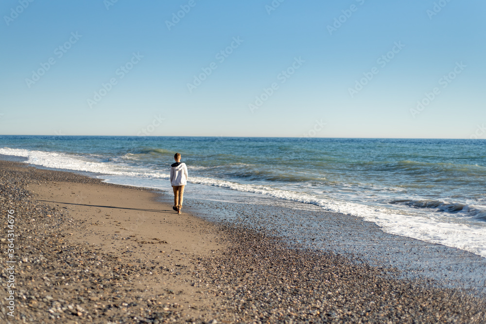 Young teen boy walking along shoreline of beach