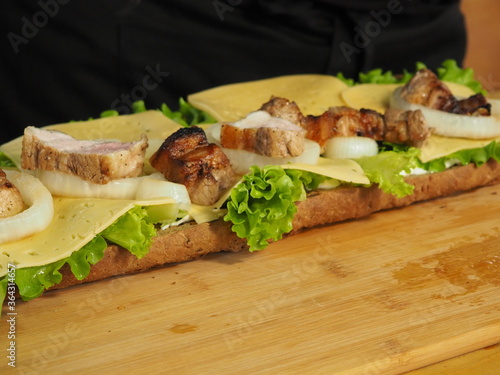 the chef slices and puts the meat on a mega sandwich with salad leaves.