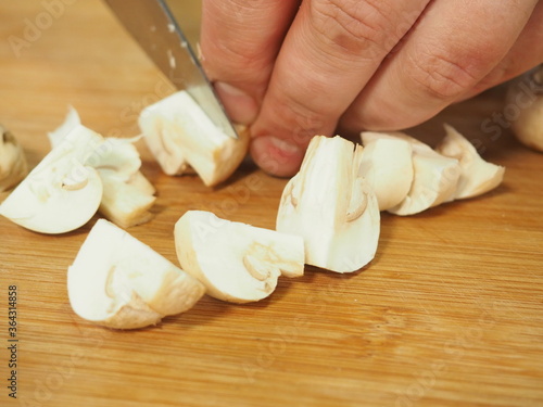 the cook slices the mushrooms with a knife on a wooden Board. slicing mushrooms