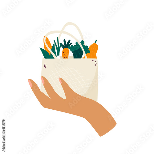 Female hand holding reusable eco bag with organic vegetables.