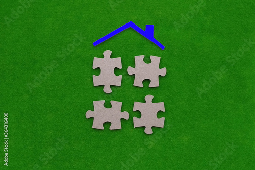 Four pieces of cardboard puzzles, the roof of the house is blue on a green background. Real estate, shared ownership.