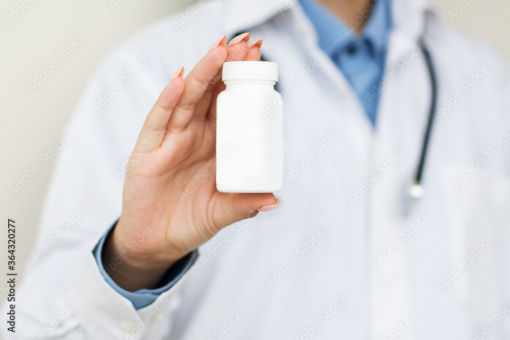 Physician medicine doctor or pharmacist sitting at worktable, holding or showing bottle of pills in hand and writing prescription on special form. Medical care, pharmacy or health insurance concept Physician medicine doctor or pharmacist sitting at worktable, holding or showing bottle of pills in hand and writing prescription on special form. Medical care, pharmacy or health insurance concept