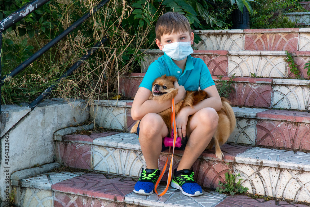 Coronavirus covid-19 concept. A little children boy in a medical mask walks with a dog. New reality. Children wearing medical face mask outdoor