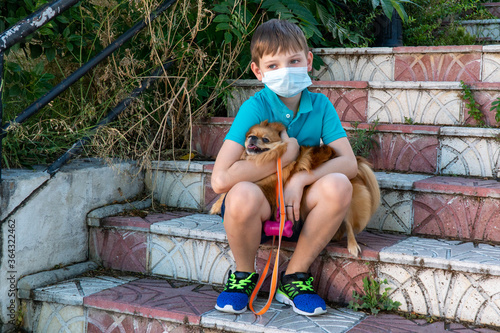 Obraz na płótnie Coronavirus covid-19 concept. A little children boy in a medical mask walks with a dog. New reality. Children wearing medical face mask outdoor w salonie