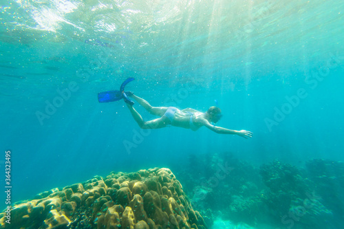 Snorkeler female in Ko Surin Marine National Park, underwater scene with sunrays. Woman snorkeling apnea in white bikini in reef of Surin Islands, Andaman Sea, North of Phuket, Phang Nga in Thailand.