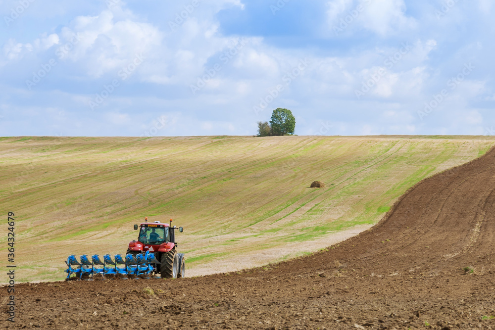 Fototapeta premium A tractor with a large plow plows a field. Tractor with agricultural attachment.
