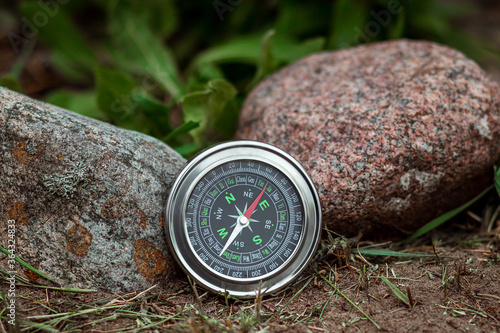Magnetic silver compass on a background of greenery. The concept of travel, finding a way, vacation. Copy space.